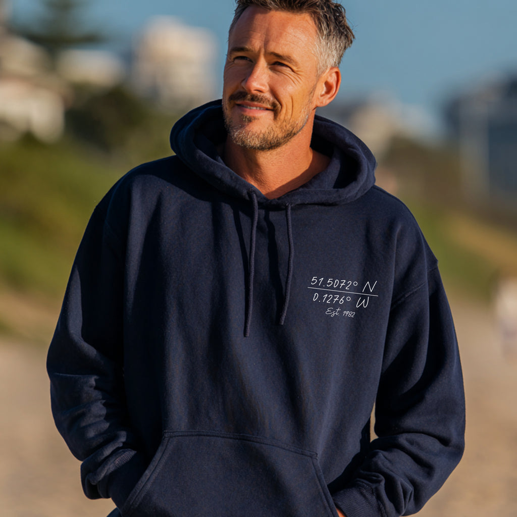 Man wearing a navy blue hoodie with embroidered text, standing outdoors.