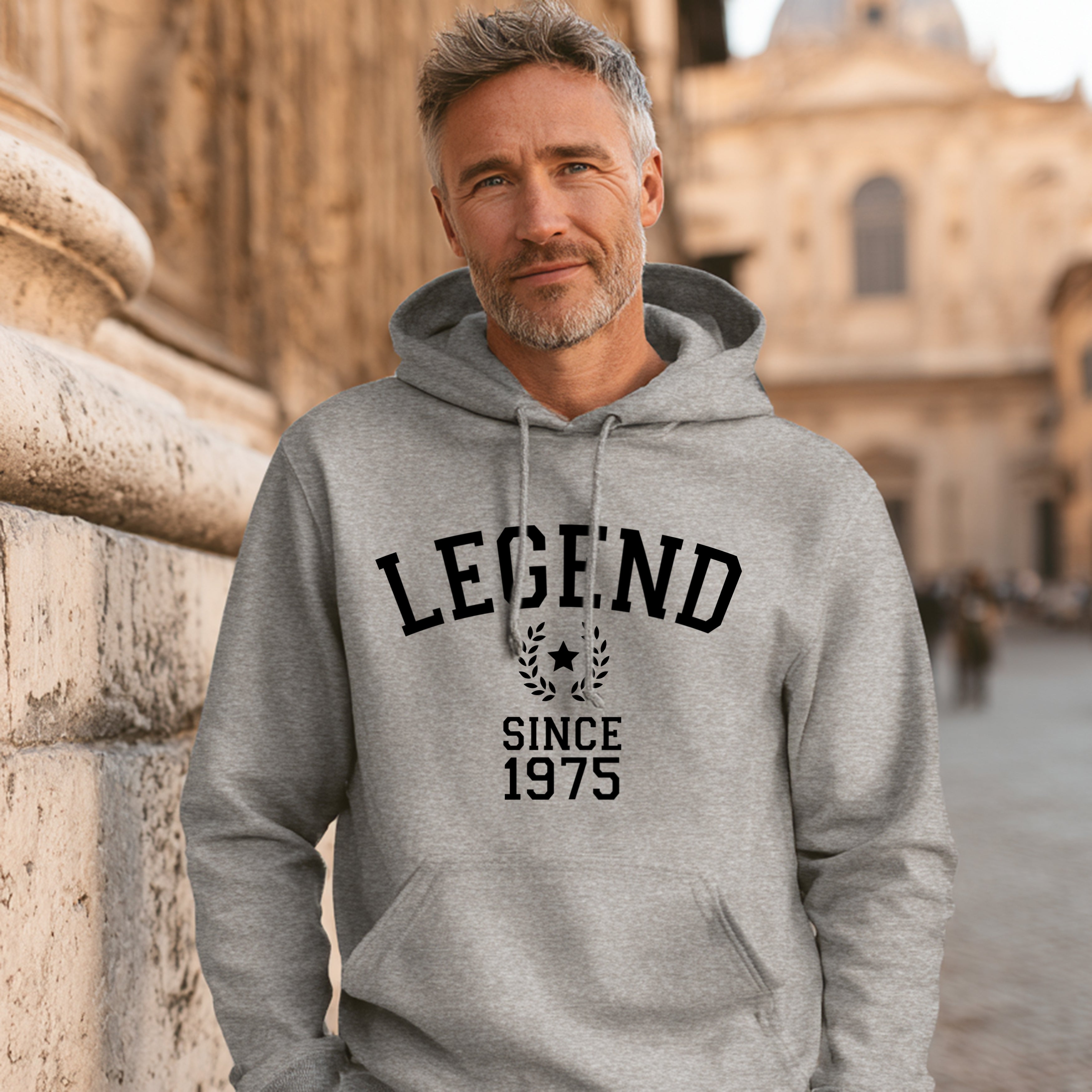 Man wearing a gray hoodie with 'LEGEND SINCE 1975' text, standing in front of stone architecture.